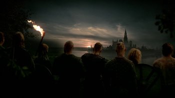 Movie still from “Vikings” (2013), created by Michael Hirst – A group of people sitting in front of a castle; Wide shot, Low angle