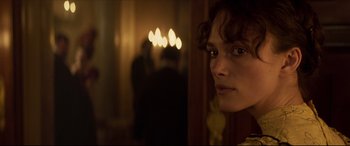 Movie still from “Colette” (2018), directed by Wash Westmoreland – A woman standing next to a wall with candles in the background; Close Up shot, Over the shoulder angle