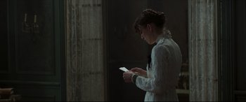 Movie still from “Colette” (2018), directed by Wash Westmoreland – A woman in a white dress holding a piece of paper; Medium shot, Over the shoulder angle
