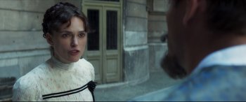 Movie still from “Colette” (2018), directed by Wash Westmoreland – A woman in a white dress standing in front of a building; Close Up shot, Over the shoulder angle