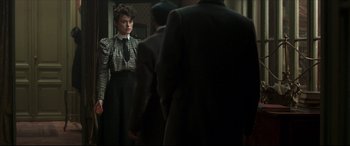 Movie still from “Colette” (2018), directed by Wash Westmoreland – A woman standing in front of a man in a suit and tie; Medium shot, Over the shoulder angle