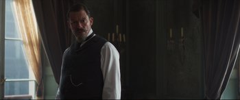 Movie still from “Colette” (2018), directed by Wash Westmoreland – A man with a beard wearing a white shirt and a black vest; Medium shot, Low angle