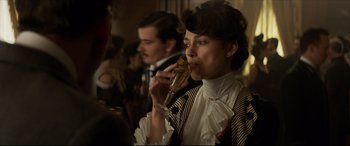 Movie still from “Colette” (2018), directed by Wash Westmoreland – A woman drinking a glass of champagne at a party; Close Up shot, Over the shoulder angle