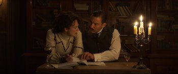Movie still from “Colette” (2018), directed by Wash Westmoreland – A man and a woman sitting at a table reading; Medium shot, Low angle