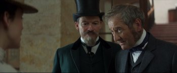Movie still from “Colette” (2018), directed by Wash Westmoreland – A man in a top hat and a man in a suit; Close Up shot, Over the shoulder angle