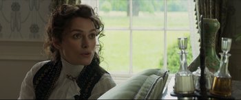 Movie still from “Colette” (2018), directed by Wash Westmoreland – A woman sitting on a couch in front of a window; Close Up shot, Over the shoulder angle