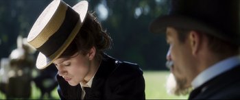 Movie still from “Colette” (2018), directed by Wash Westmoreland – A woman with a hat sitting in the grass; Close Up shot, Over the shoulder angle
