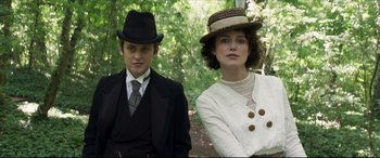 Movie still from “Colette” (2018), directed by Wash Westmoreland – A man and a woman wearing hats in a forest; Medium shot, Low angle
