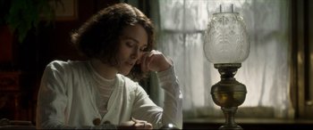 Movie still from “Colette” (2018), directed by Wash Westmoreland – A woman sitting in front of a lamp in a room; Close Up shot, High angle