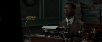 Movie still from “Colette” (2018), directed by Wash Westmoreland – A man sitting at a typewriter in a room; Medium shot, Low angle