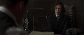 Movie still from “Colette” (2018), directed by Wash Westmoreland – A person sitting at a table in a suit; Medium shot, Over the shoulder angle