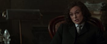 Movie still from “Colette” (2018), directed by Wash Westmoreland – A woman sitting in a chair wearing a black suit; Close Up shot, Over the shoulder angle