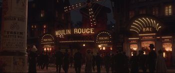 Movie still from “Colette” (2018), directed by Wash Westmoreland – A group of people standing in front of a moulin rouge sign; Extreme Wide shot, Low angle