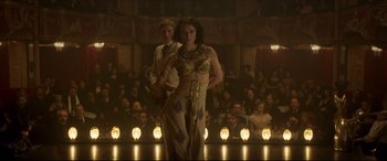 Movie still from “Colette” (2018), directed by Wash Westmoreland – A man and a woman are standing in front of a group of people; Wide shot, Over the shoulder angle