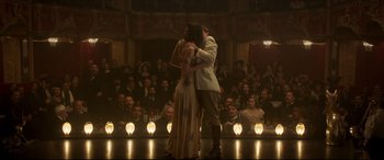 Movie still from “Colette” (2018), directed by Wash Westmoreland – A man and a woman embracing in front of an audience; Wide shot, Low angle