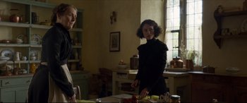 Movie still from “Colette” (2018), directed by Wash Westmoreland – A woman standing in front of a counter cutting food; Medium shot, Over the shoulder angle