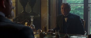 Movie still from “Colette” (2018), directed by Wash Westmoreland – A man sitting at a dinner table smoking a cigarette; Medium shot, Over the shoulder angle