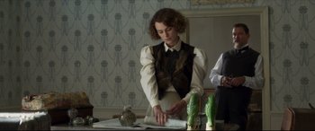 Movie still from “Colette” (2018), directed by Wash Westmoreland – A woman is cutting paper at a table; Medium shot, Over the shoulder angle