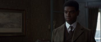 Movie still from “Colette” (2018), directed by Wash Westmoreland – A man wearing a suit and tie standing in front of a window; Close Up shot, Over the shoulder angle