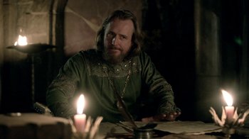 Movie still from “Vikings” (2013), created by Michael Hirst – A man sitting at a table with a lit candle; Medium shot, Over the shoulder angle