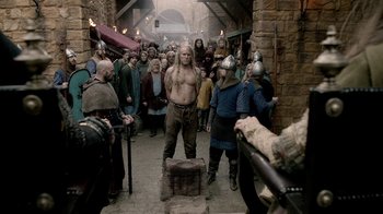 Movie still from “Vikings” (2013), created by Michael Hirst – A group of men in medieval garb are standing in front of a crowd; Wide shot, Over the shoulder angle