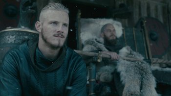 Movie still from “Vikings” (2013), created by Michael Hirst – A man with blonde hair sitting next to another man with a beard; Close Up shot, Low angle