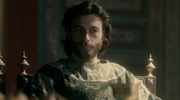 Movie still from “Vikings” (2013), created by Michael Hirst – A man with long hair and a beard is holding a wine glass; Medium shot, Over the shoulder angle