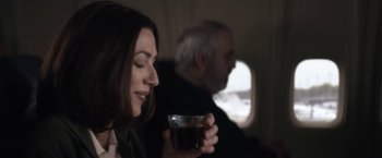 Movie still from “Come Sunday” (2018), directed by Joshua Marston – A woman holding a cup of coffee while sitting next to an older man; Close Up shot, Over the shoulder angle
