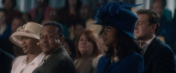 Movie still from “Come Sunday” (2018), directed by Joshua Marston – A woman in a blue hat is standing next to a man; Close Up shot, Over the shoulder angle