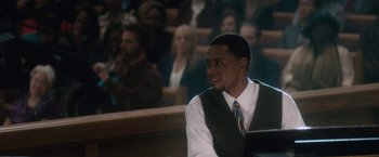 Movie still from “Come Sunday” (2018), directed by Joshua Marston – A man sitting in front of a group of people; Medium shot, Over the shoulder angle