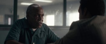 Movie still from “Come Sunday” (2018), directed by Joshua Marston – An older man sitting at a table in front of a window; Close Up shot, Over the shoulder angle