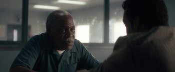 Movie still from “Come Sunday” (2018), directed by Joshua Marston – An older man sitting in front of another man in front of a window; Close Up shot, Over the shoulder angle