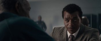 Movie still from “Come Sunday” (2018), directed by Joshua Marston – A person wearing a suit and tie; Close Up shot, Over the shoulder angle