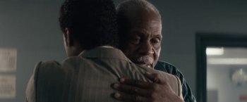 Movie still from “Come Sunday” (2018), directed by Joshua Marston – Two men are hugging each other in a dark room; Close Up shot, Over the shoulder angle