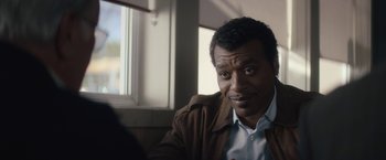 Movie still from “Come Sunday” (2018), directed by Joshua Marston – A person sitting in front of a window; Close Up shot, Over the shoulder angle