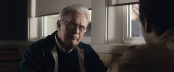 Movie still from “Come Sunday” (2018), directed by Joshua Marston – An older man with white hair and wearing glasses; Close Up shot, Over the shoulder angle