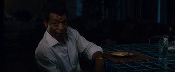 Movie still from “Come Sunday” (2018), directed by Joshua Marston – A man sitting at a table with a plate of food; Medium shot, Over the shoulder angle