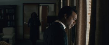 Movie still from “Come Sunday” (2018), directed by Joshua Marston – A man standing in a room next to a window; Close Up shot, Over the shoulder angle