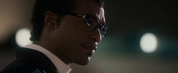 Movie still from “Come Sunday” (2018), directed by Joshua Marston – A person wearing glasses and a suit; Close Up shot, Low angle