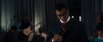 Movie still from “Come Sunday” (2018), directed by Joshua Marston – A man in a suit and glasses looking at his cell phone; Close Up shot, Over the shoulder angle