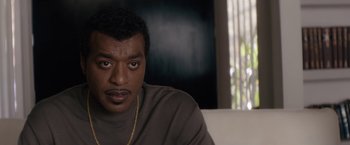 Movie still from “Come Sunday” (2018), directed by Joshua Marston – A person sitting on a couch; Close Up shot, High angle