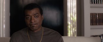 Movie still from “Come Sunday” (2018), directed by Joshua Marston – A person sitting on a couch; Close Up shot, High angle