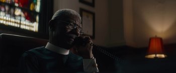 Movie still from “Come Sunday” (2018), directed by Joshua Marston – An older man talking on a phone while wearing a suit; Close Up shot, Low angle