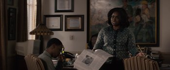 Movie still from “Come Sunday” (2018), directed by Joshua Marston – A woman standing next to a man holding a newspaper; Medium shot, Over the shoulder angle