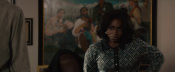 Movie still from “Come Sunday” (2018), directed by Joshua Marston – A woman in front of a painting in a room; Medium shot, Over the shoulder angle
