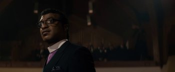 Movie still from “Come Sunday” (2018), directed by Joshua Marston – A man wearing a suit and tie standing in front of a crowd; Close Up shot, Low angle