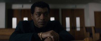 Movie still from “Come Sunday” (2018), directed by Joshua Marston – A person sitting in a room; Close Up shot, Low angle