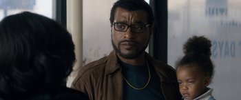 Movie still from “Come Sunday” (2018), directed by Joshua Marston – A person wearing glasses and a brown jacket; Close Up shot, Over the shoulder angle