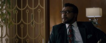 Movie still from “Come Sunday” (2018), directed by Joshua Marston – A man in a suit and tie looking off into the distance; Close Up shot, Over the shoulder angle
