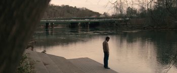 Movie still from “Come Sunday” (2018), directed by Joshua Marston – A man standing on a dock near a body of water; Extreme Wide shot, High angle